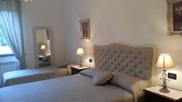 A hotel room with two beds, a chandelier, a mirror, and a framed picture on the wall.