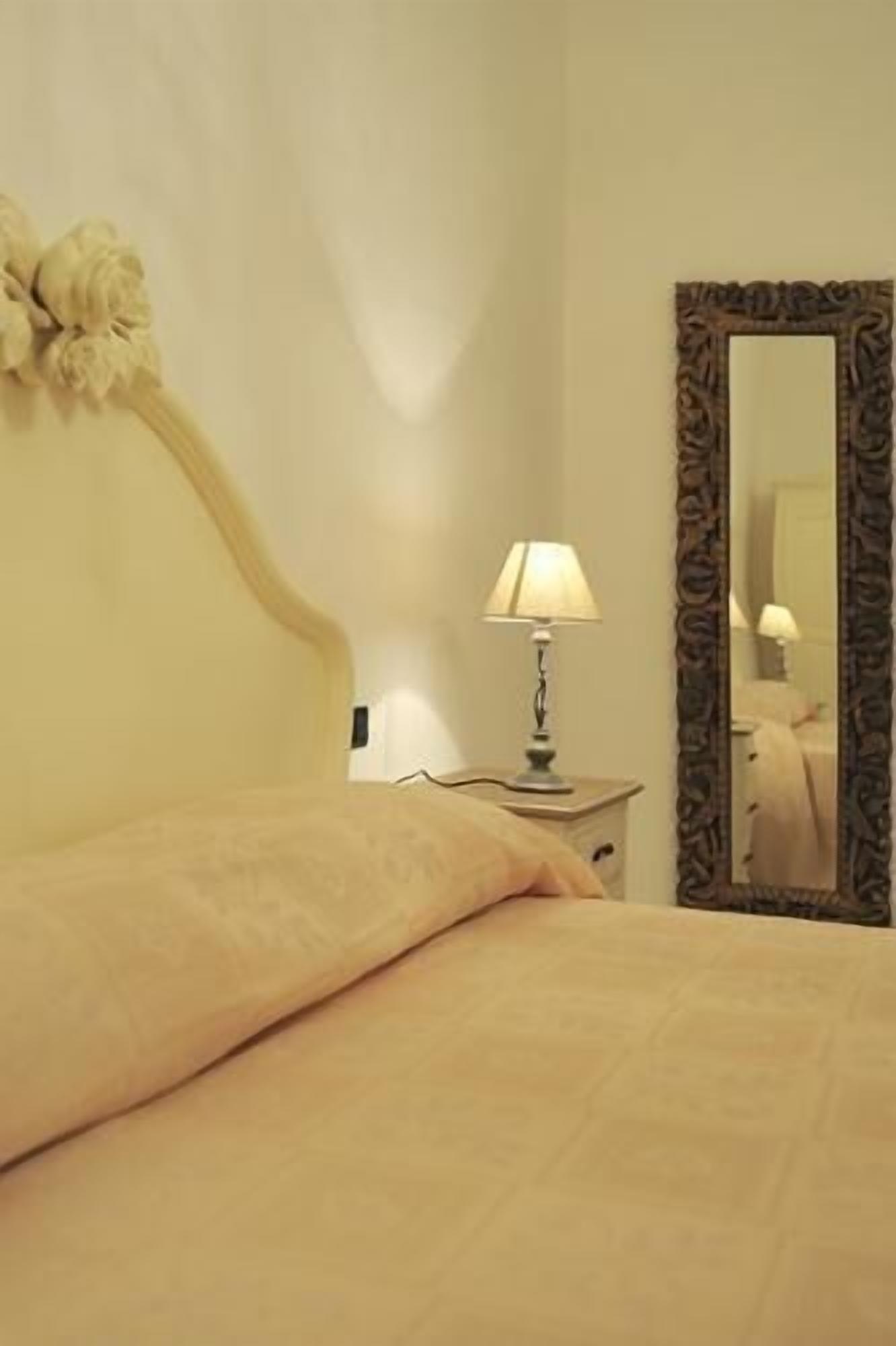 Una cama bien hecha con una lámpara y un espejo sobre una mesita de noche.