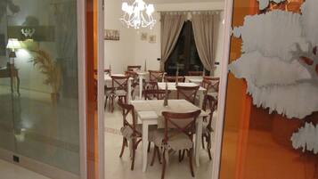 A dining area with multiple tables and chairs, a chandelier, and a large window with curtains.