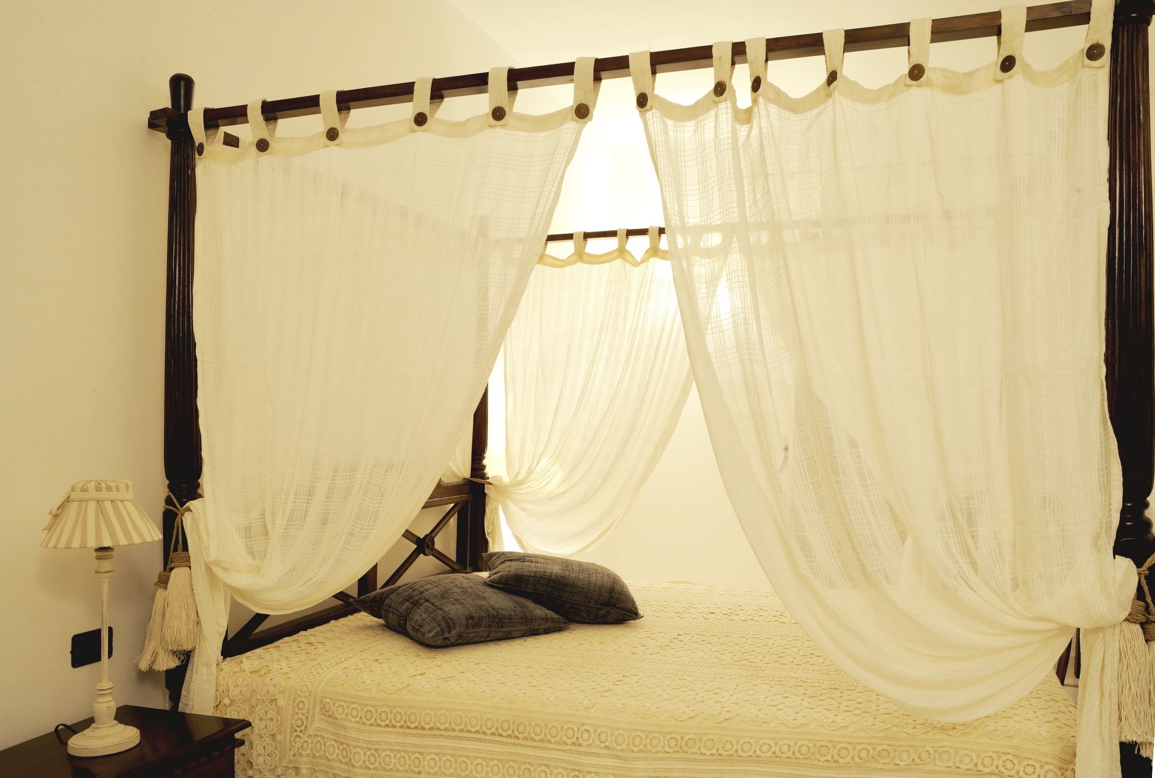 Un lit à baldaquin, une table de chevet avec une lampe et un interrupteur fixé au mur.