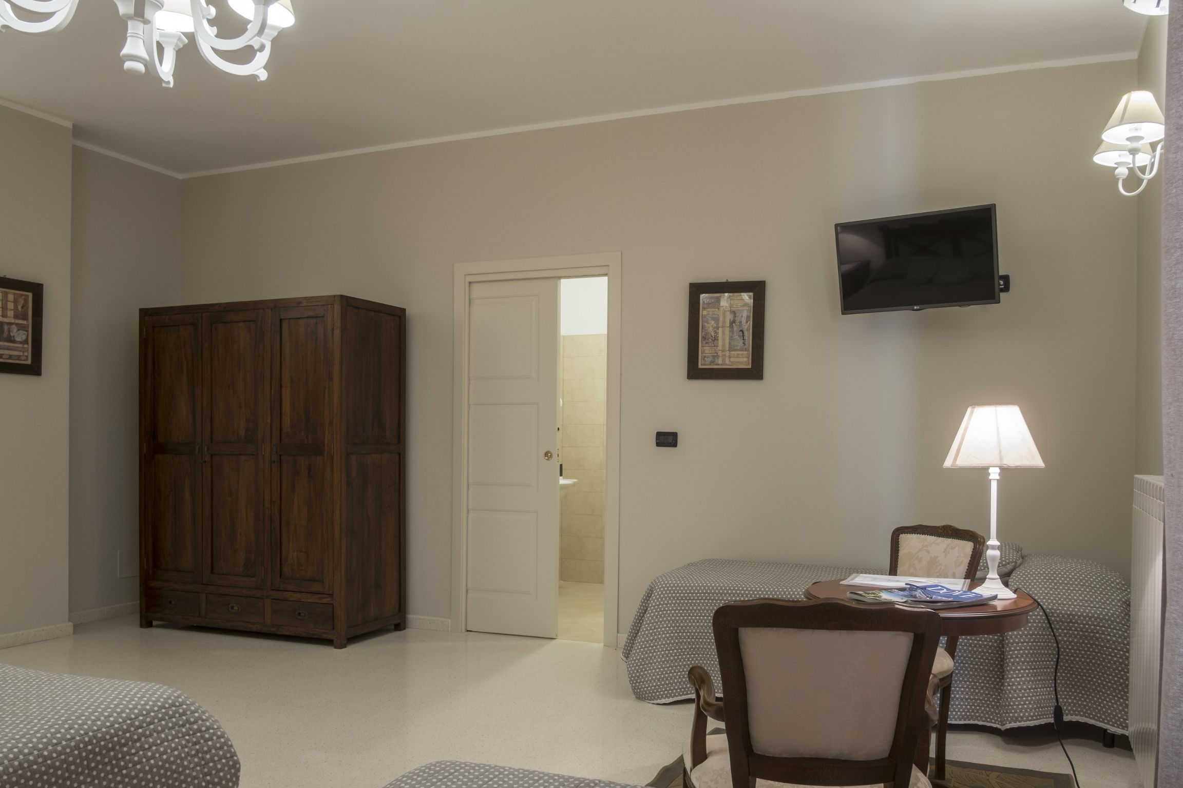 A hotel room with two beds, a wooden wardrobe, a television, and a desk with a lamp.