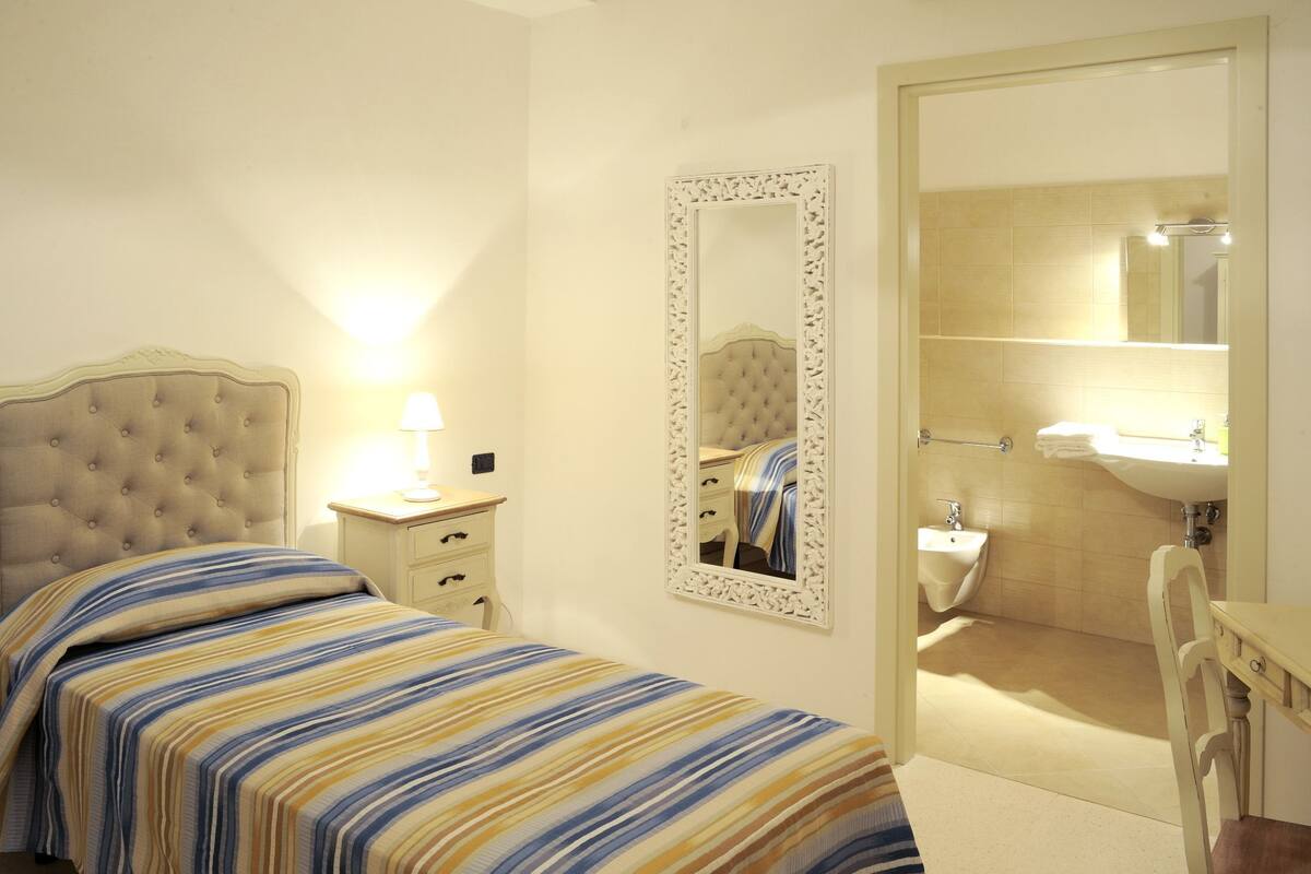 A bedroom with a bed, bedside table, lamp, and a mirror.