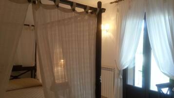 Un dormitorio con cama con dosel, cortinas translúcidas y vistas al exterior a través de una ventana.