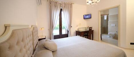 A bedroom with a large bed, a television on the wall, and a bathroom visible through an open door.