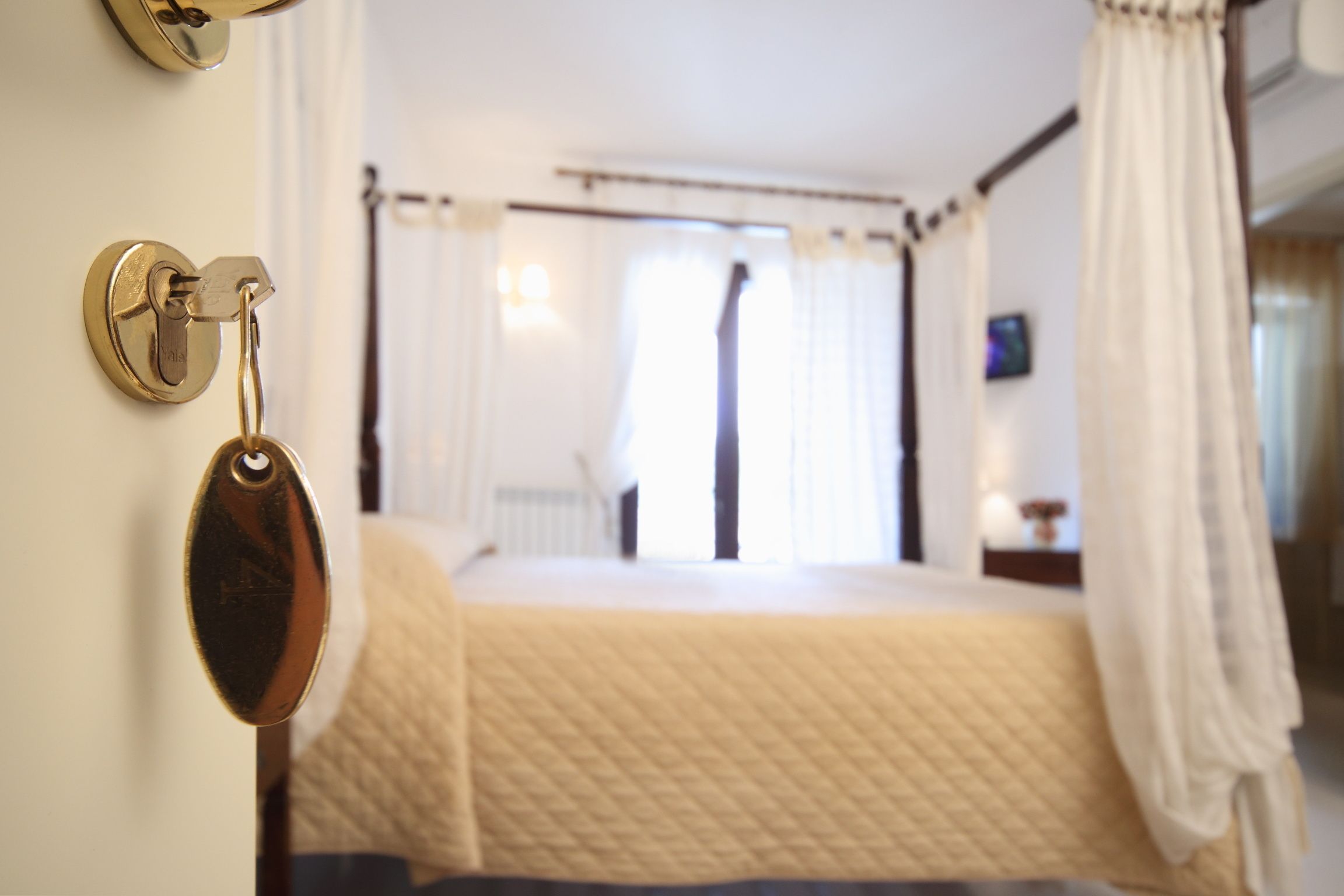 A hotel room with a bed, a bedside table, a TV, and a window with curtains.