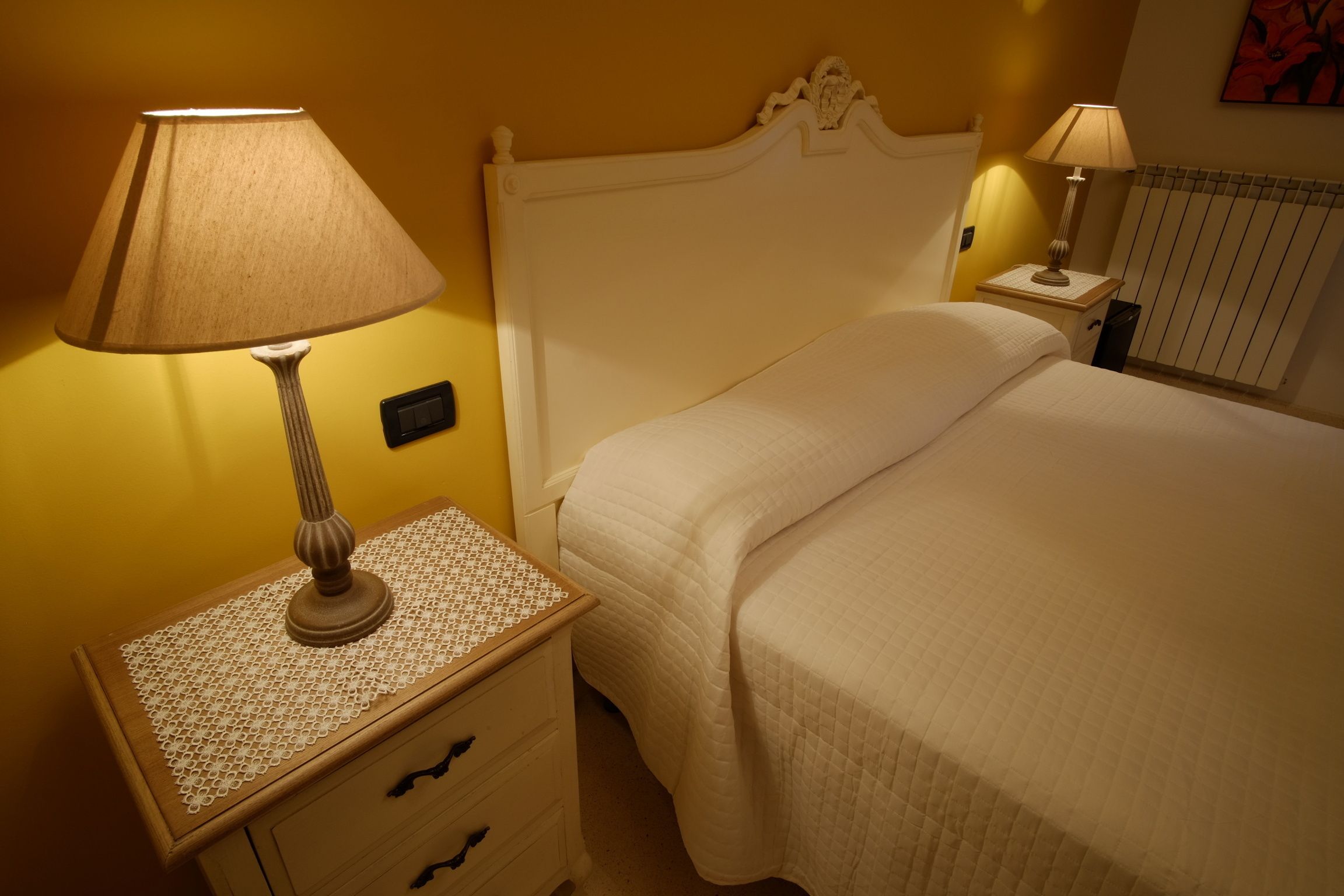 A neatly made bed with a white headboard, a bedside table with a lamp, and a wall-mounted light.