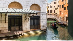 A canal with gondolas, a stone building with a covered entrance, and a bridge in the background. - Ca Maria Callas (Venice)