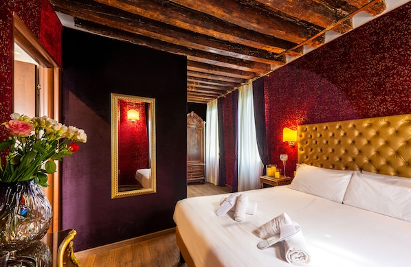 A hotel room with a large bed, a mirror, a vase with flowers, and a wooden ceiling.