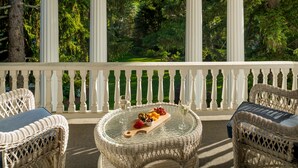 A covered outdoor seating area with wicker furniture and a glass table displaying fruit and wine glasses.