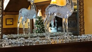 A chandelier with a deer design, a Christmas tree, and a staircase in the background.