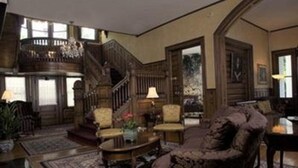 A spacious living room with a grand staircase, comfortable seating, and a large window providing natural light.