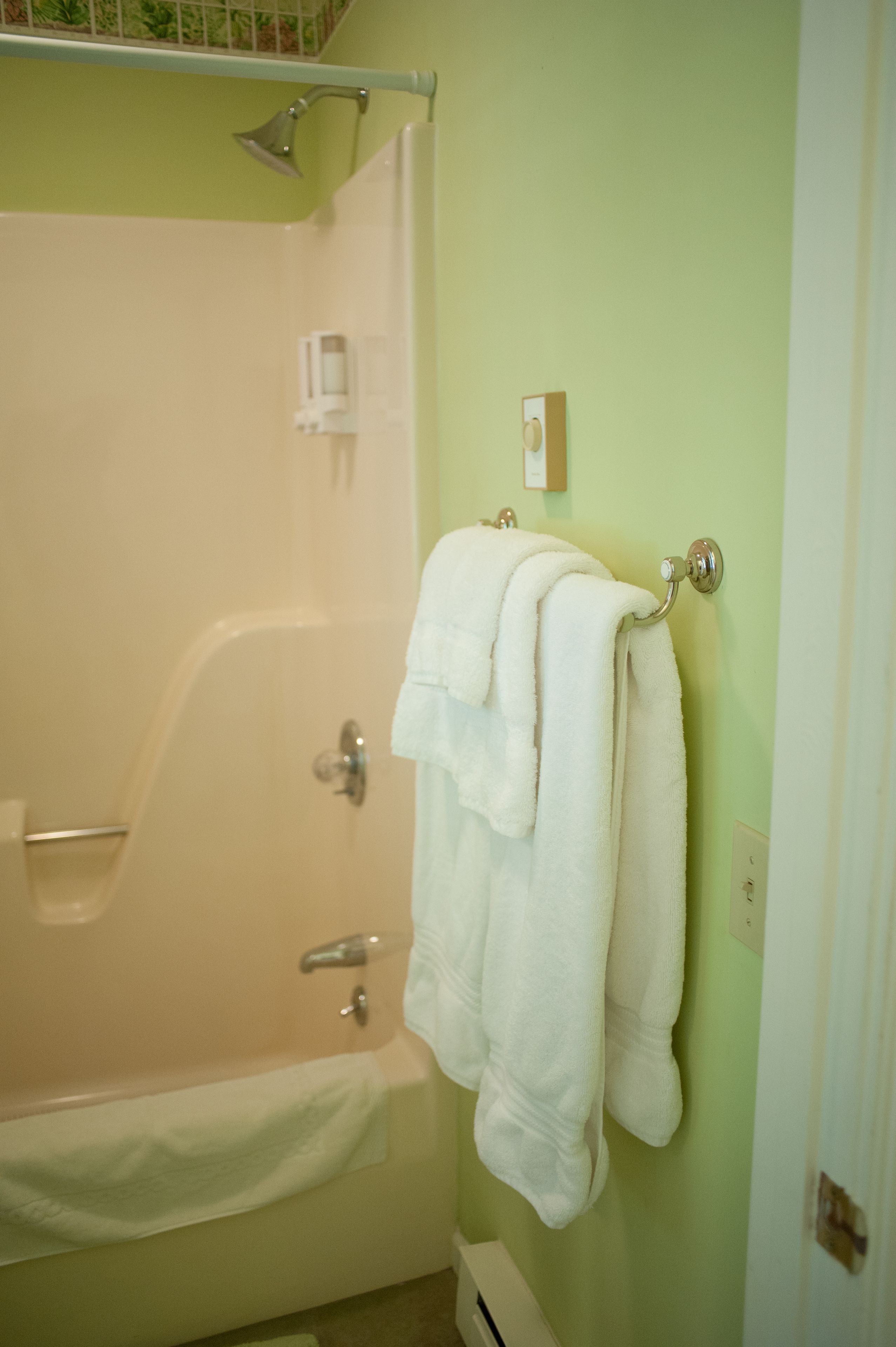 Un baño con bañera, un perchero con dos toallas y un cabezal de ducha.