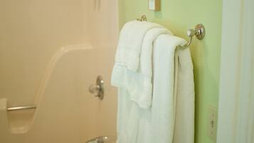 Un baño con bañera, un perchero con dos toallas y un cabezal de ducha.