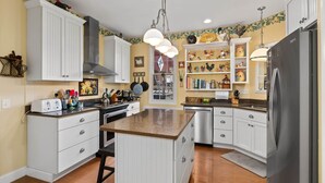 A kitchen with white cabinetry, a central island, stainless steel appliances, and decorative items on shelves.
