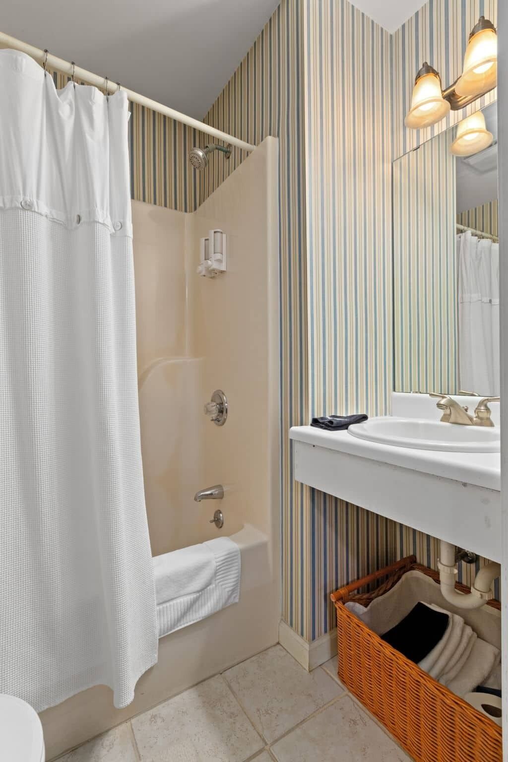 A bathroom with a shower, a bathtub, a sink, a mirror, and a wicker basket.