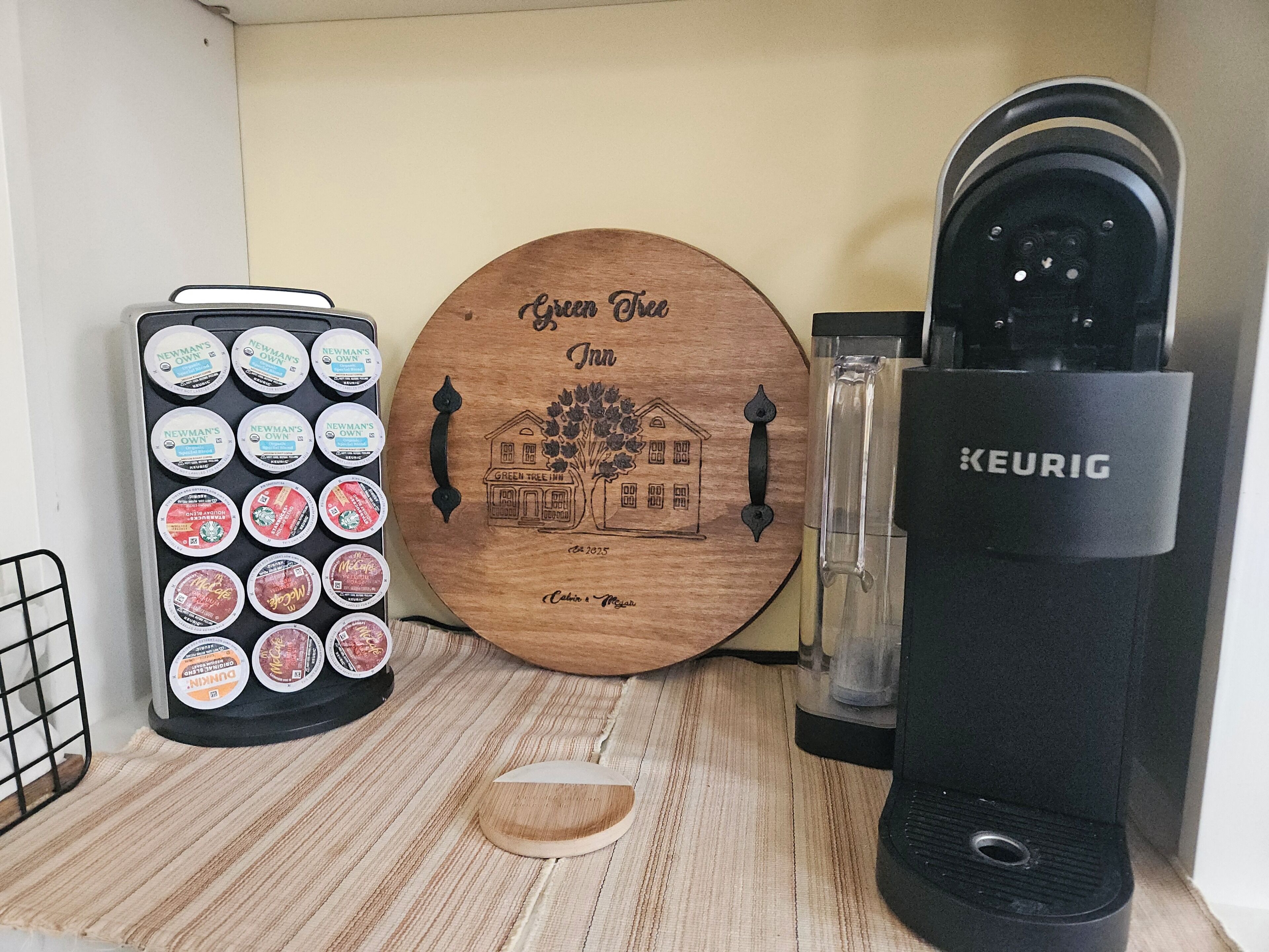 Eine Kaffeemaschine, eine Kaffeekapseln-Tablett und eine Holztafel mit der eingravierten Aufschrift 'Green Tree Inn'.