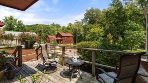 A wooden deck with outdoor furniture, a small table, and a view of a red building and trees.