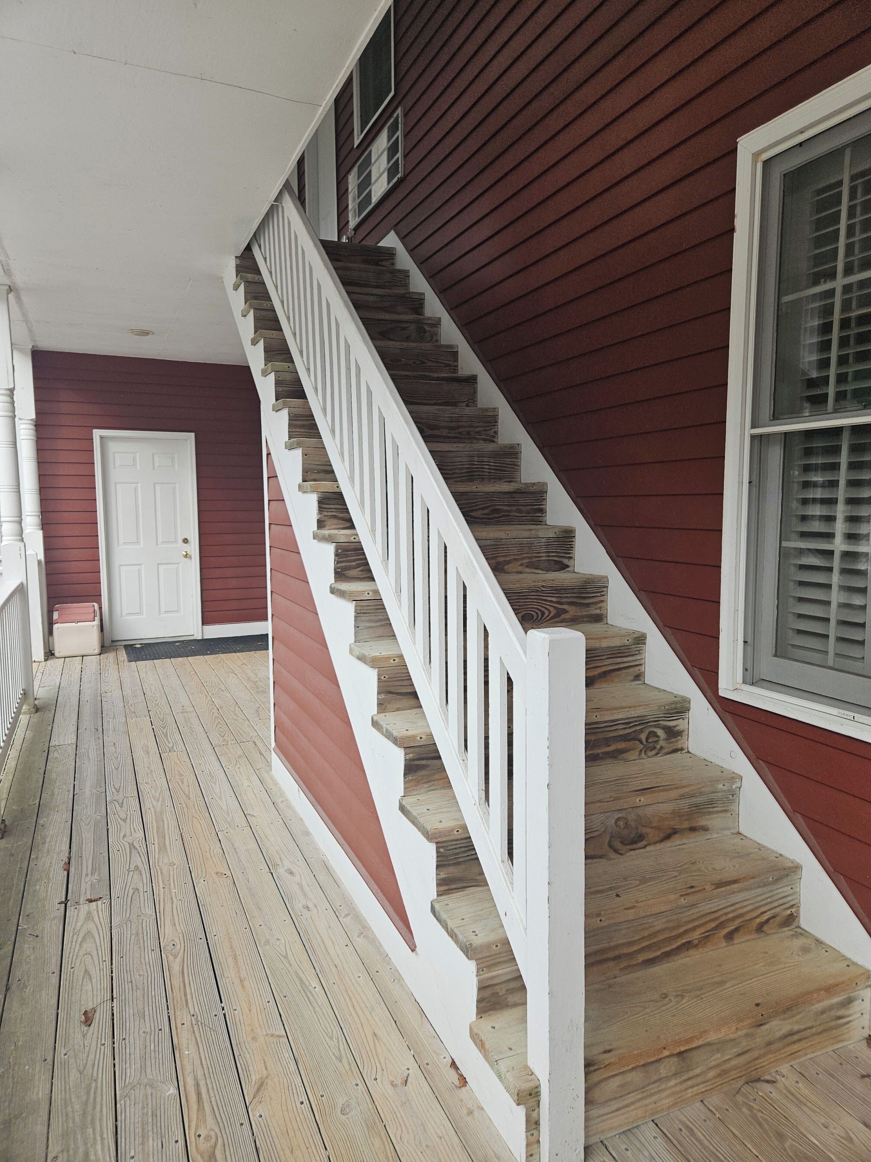 Una escalera de madera con barandillas blancas que conduce a una pared exterior roja.