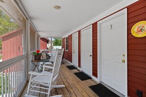 A covered porch with white chairs, a table, and a red door.