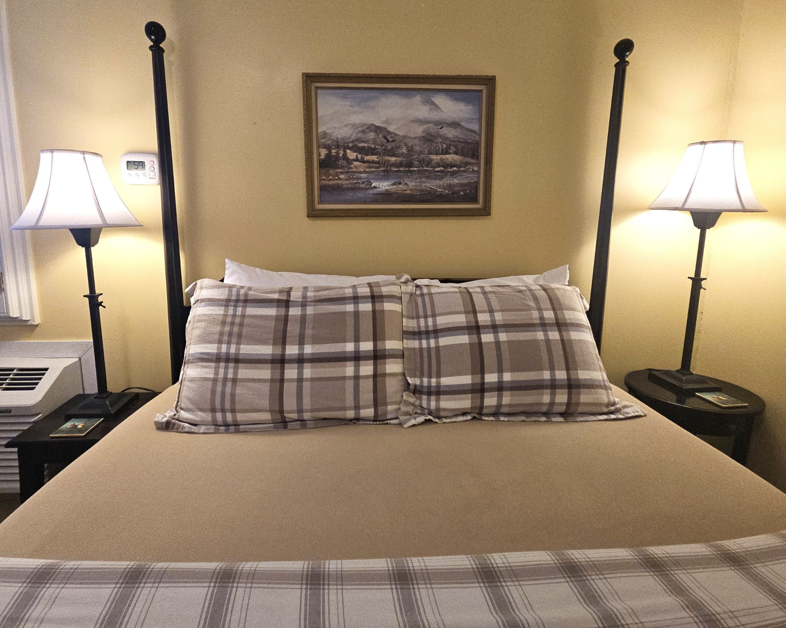 Une chambre d’hôtel avec un lit, deux tables de chevet, un tableau au mur et un thermostat.