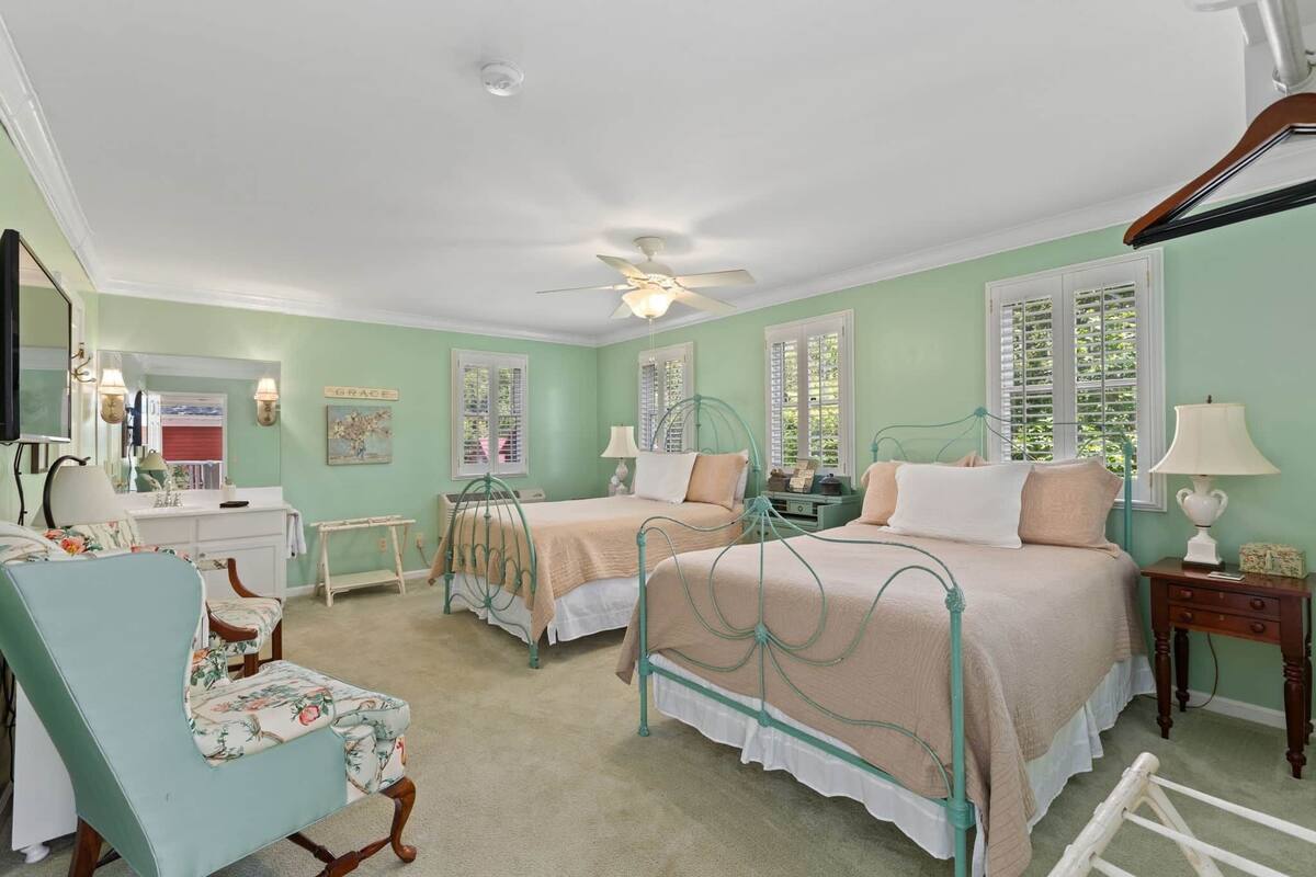 A bedroom with two beds, a vanity, a chair, and a ceiling fan.
