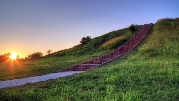 A staircase on a grassy hill with a sunset in the background.