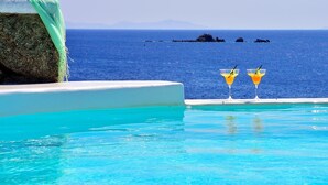 A pool with clear blue water, two martini glasses with yellow drinks, and a view of the sea and distant islands. - Mykonos Pantheon (Mykonos)