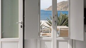 A room with a large sliding glass door leading to a balcony with a view of the sea and a mountain. - Mykonos Pantheon (Mykonos)
