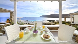 A breakfast table with a view of the sea, white wicker chairs, and a stone pillar. - Mykonos Pantheon (Mykonos)