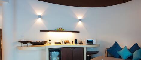 A modern room with a curved ceiling, a built-in kitchen area, a seating area with cushions, and a hanging light fixture.
