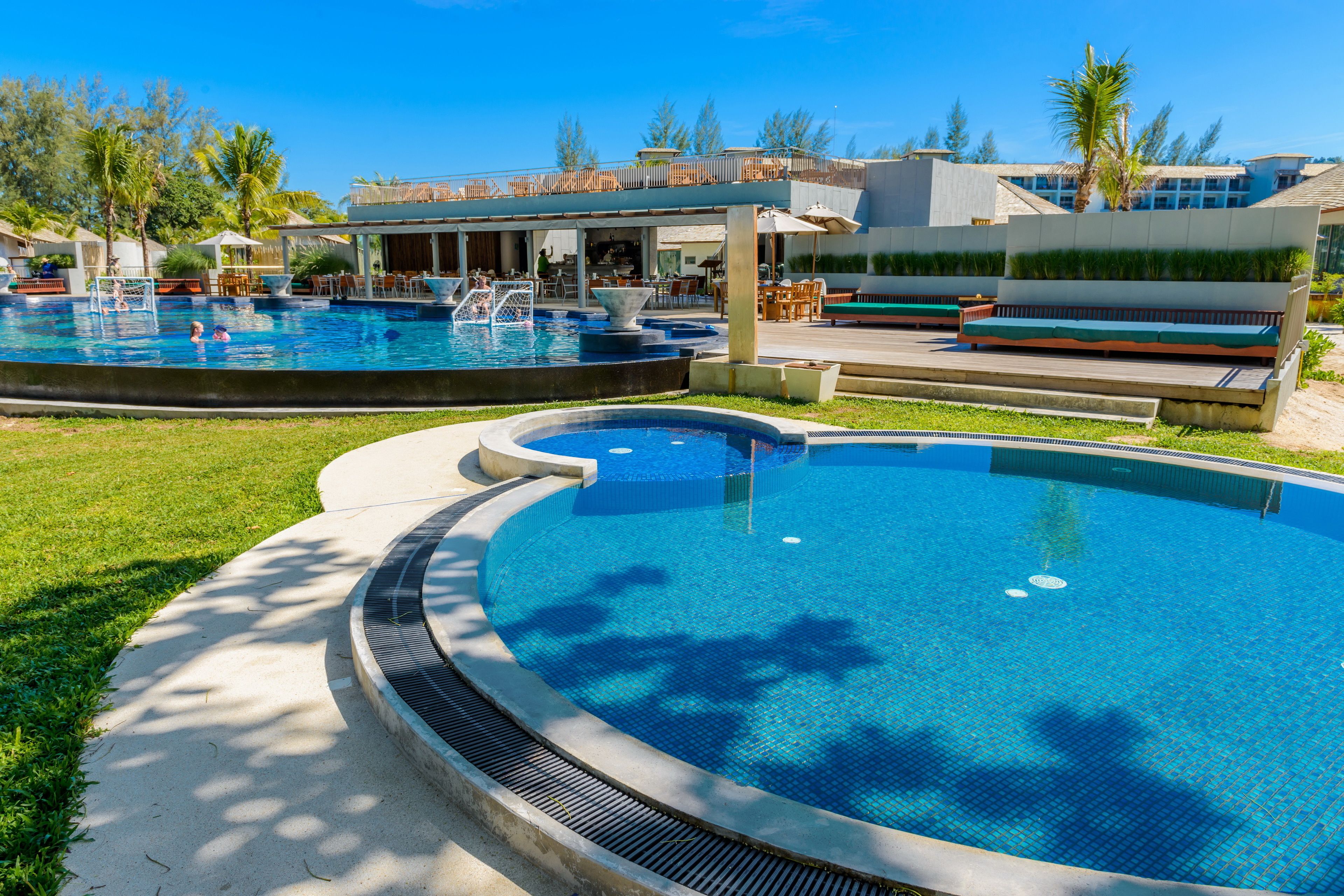 A swimming pool area with multiple pools, lounge seating, and a covered patio area.