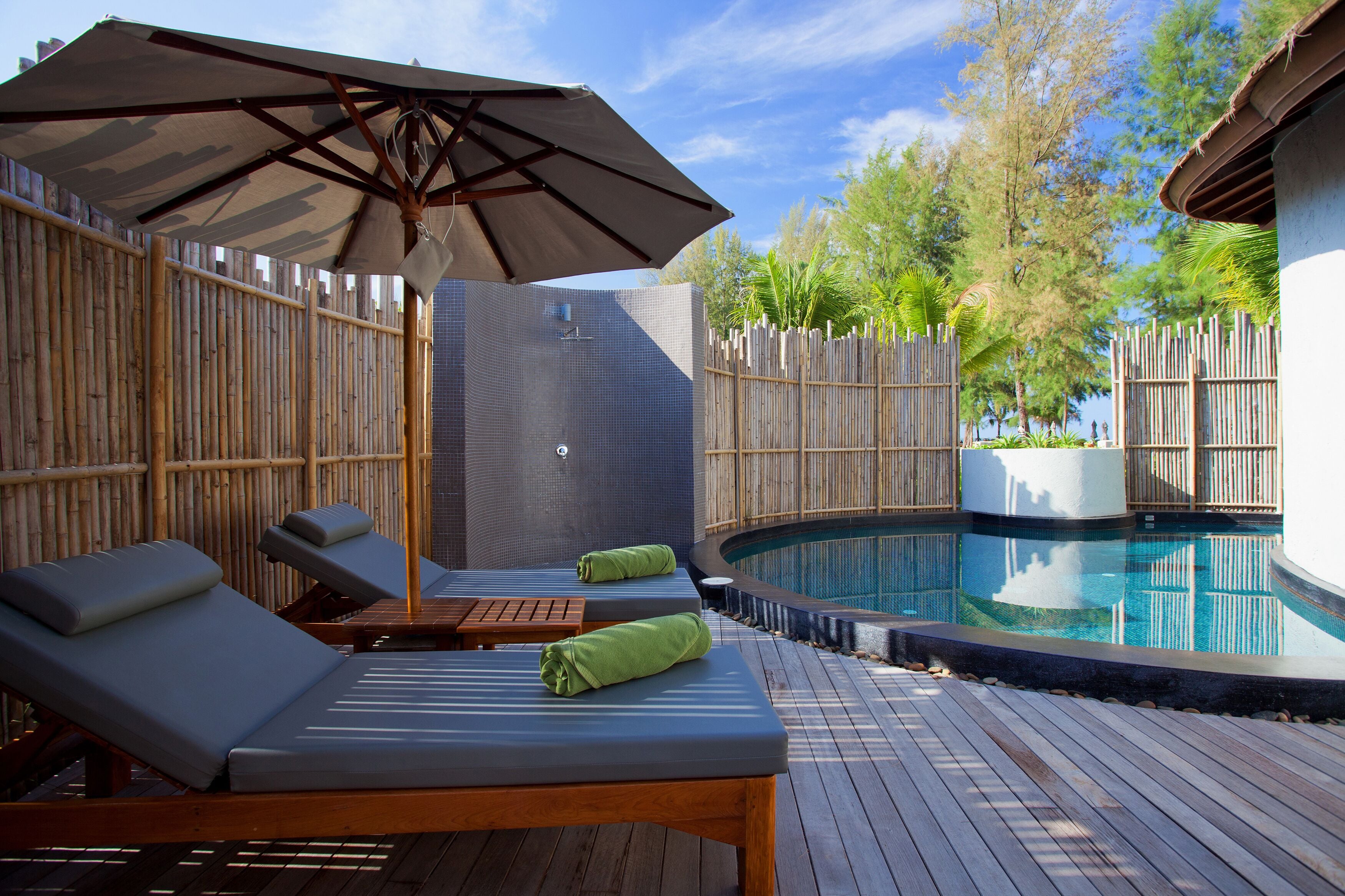 Un área junto a la piscina con sillones de descanso, una terraza de madera y una valla de bambú.