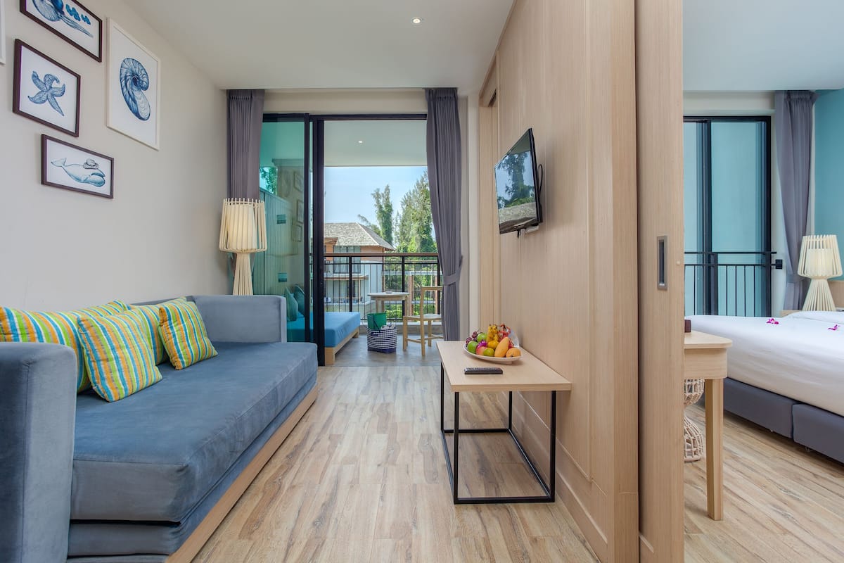 Une chambre d’hôtel moderne avec un canapé, une petite table avec des fruits, une télévision et un balcon offrant une vue.