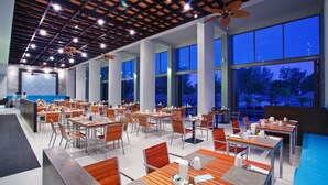 Un vaste espace dédié à la salle à manger, avec de nombreuses tables et chaises, de grandes fenêtres et un ventilateur de plafond.