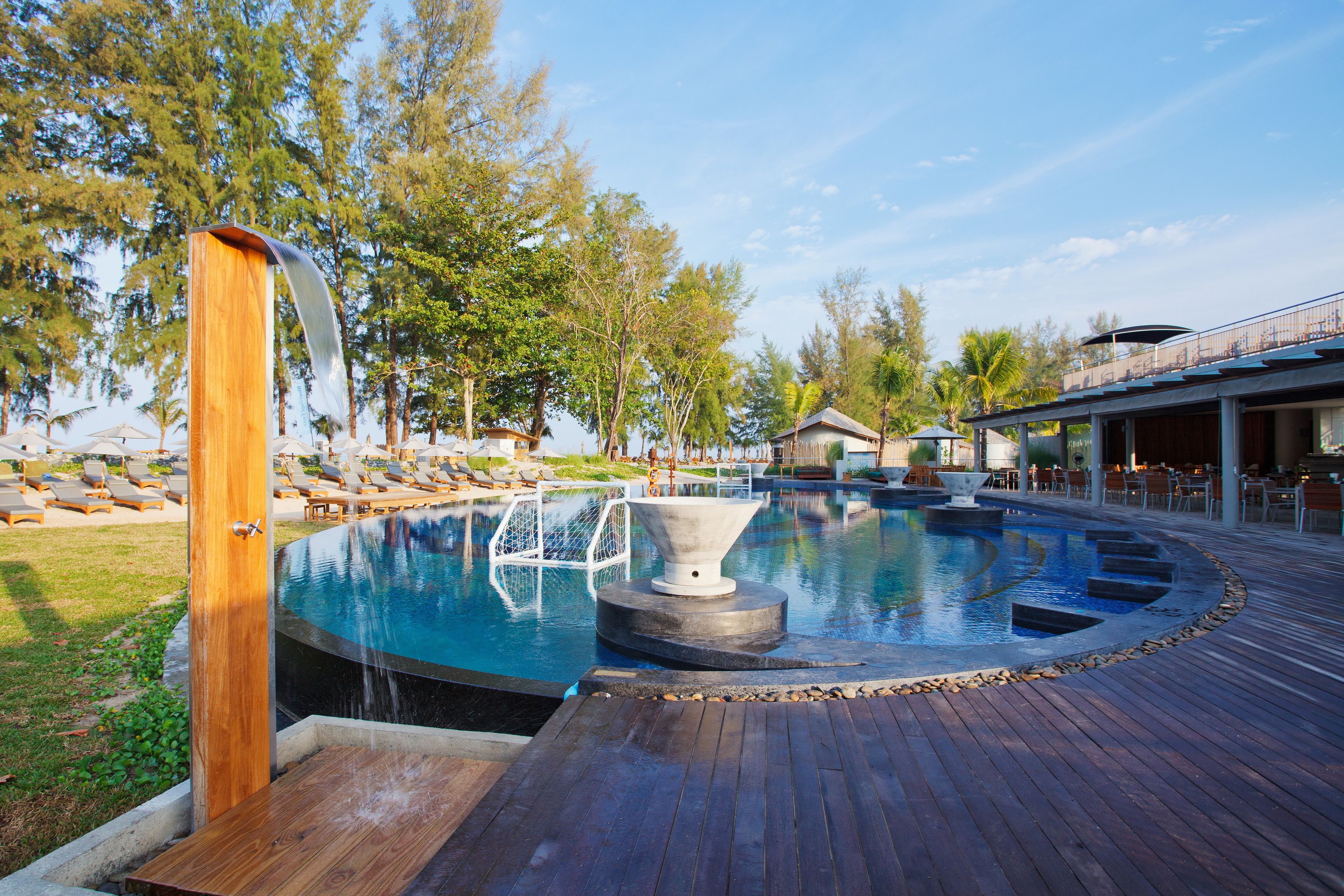 A pool area with a wooden deck, lounge chairs, and a small building in the background.