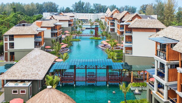 Un complexe hôtelier doté de plusieurs piscines, de bungalows sur pilotis et d’un pont central reliant les différents bâtiments.