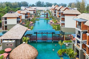Un complexe hôtelier doté de plusieurs piscines, de bungalows sur pilotis et d’un pont central reliant les différents bâtiments.