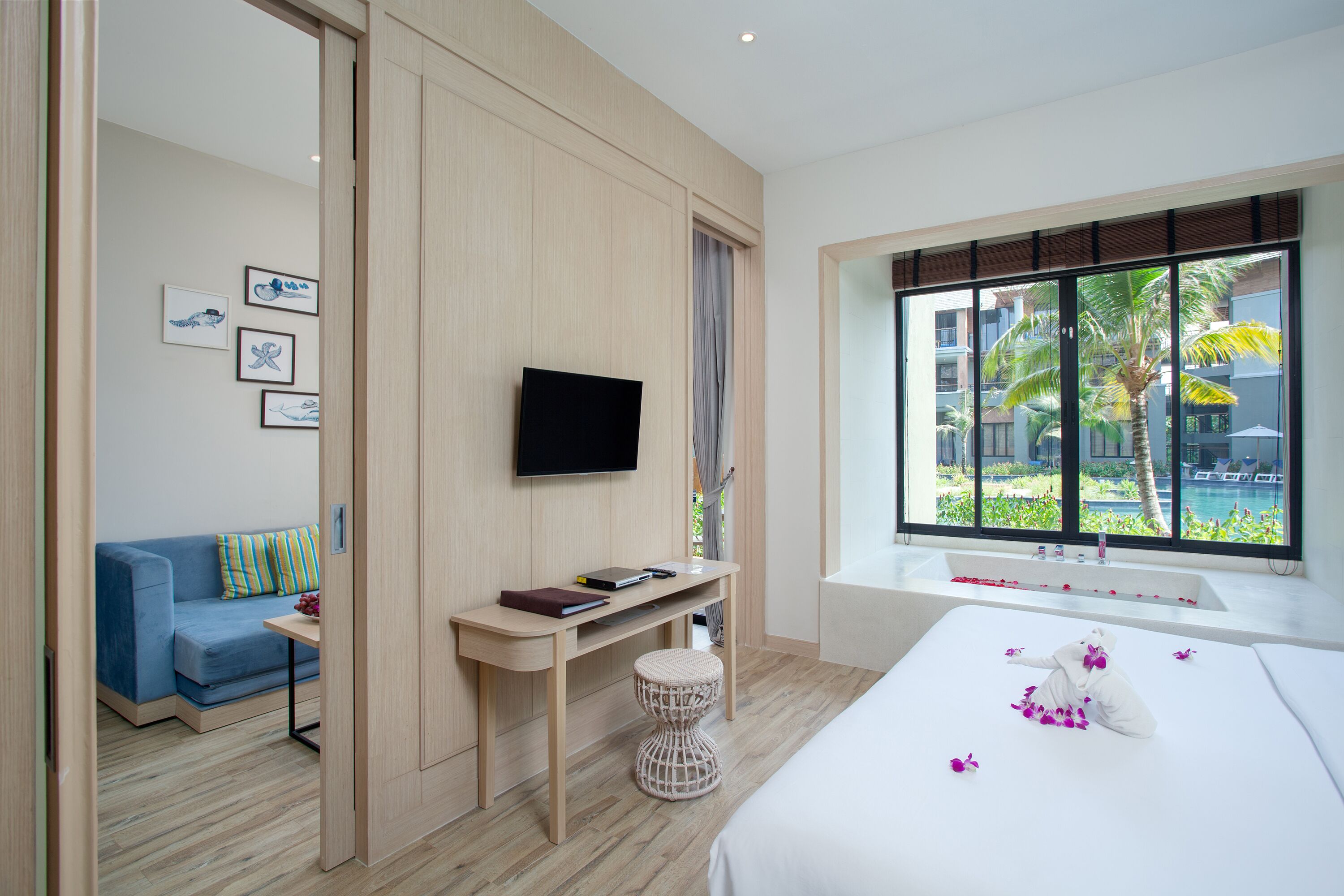 A modern hotel room with a bed, a desk, a TV, and a view of the pool and palm trees.