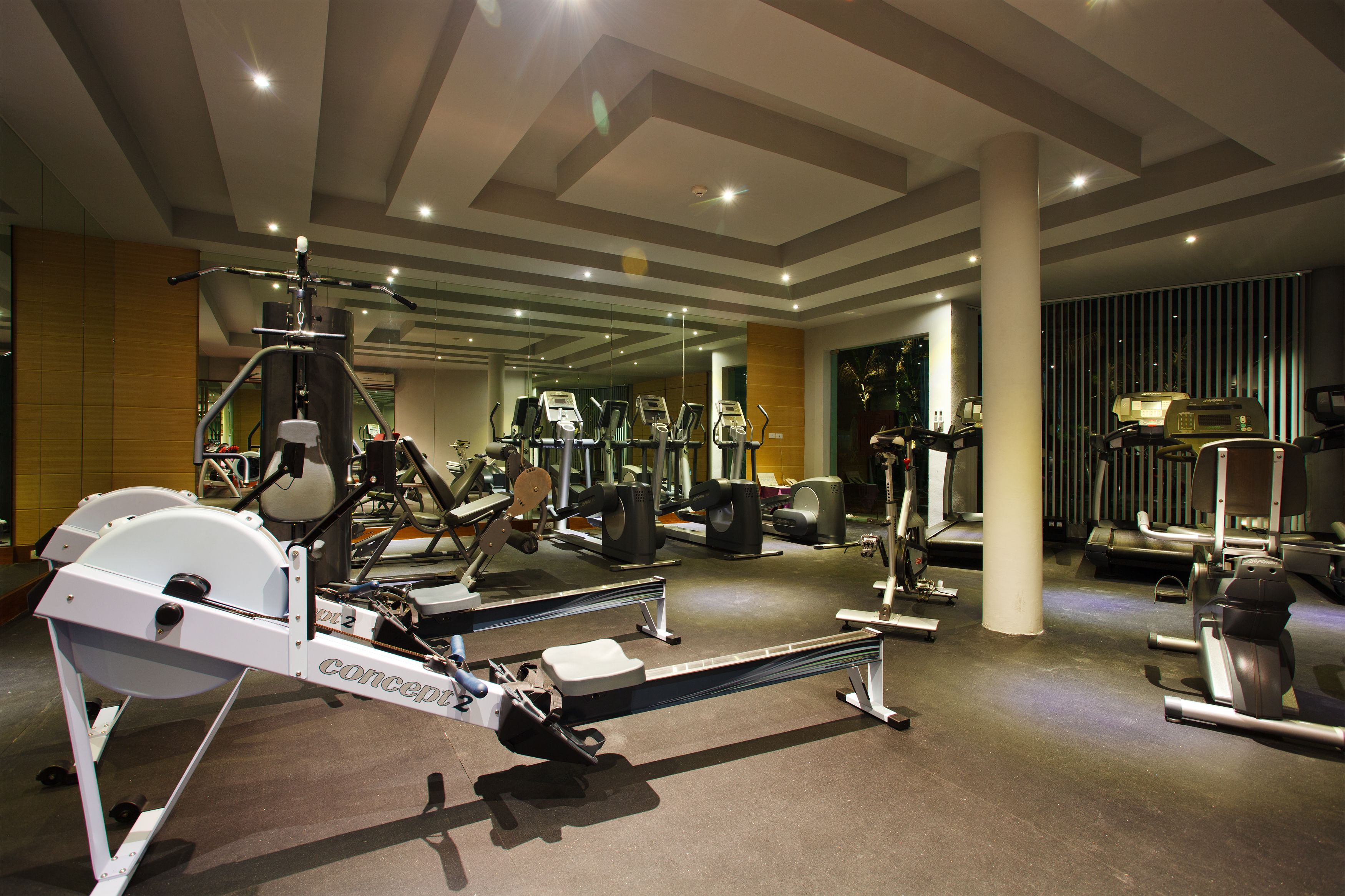 A gym with various exercise equipment, including treadmills and weight machines, and a mirrored wall.