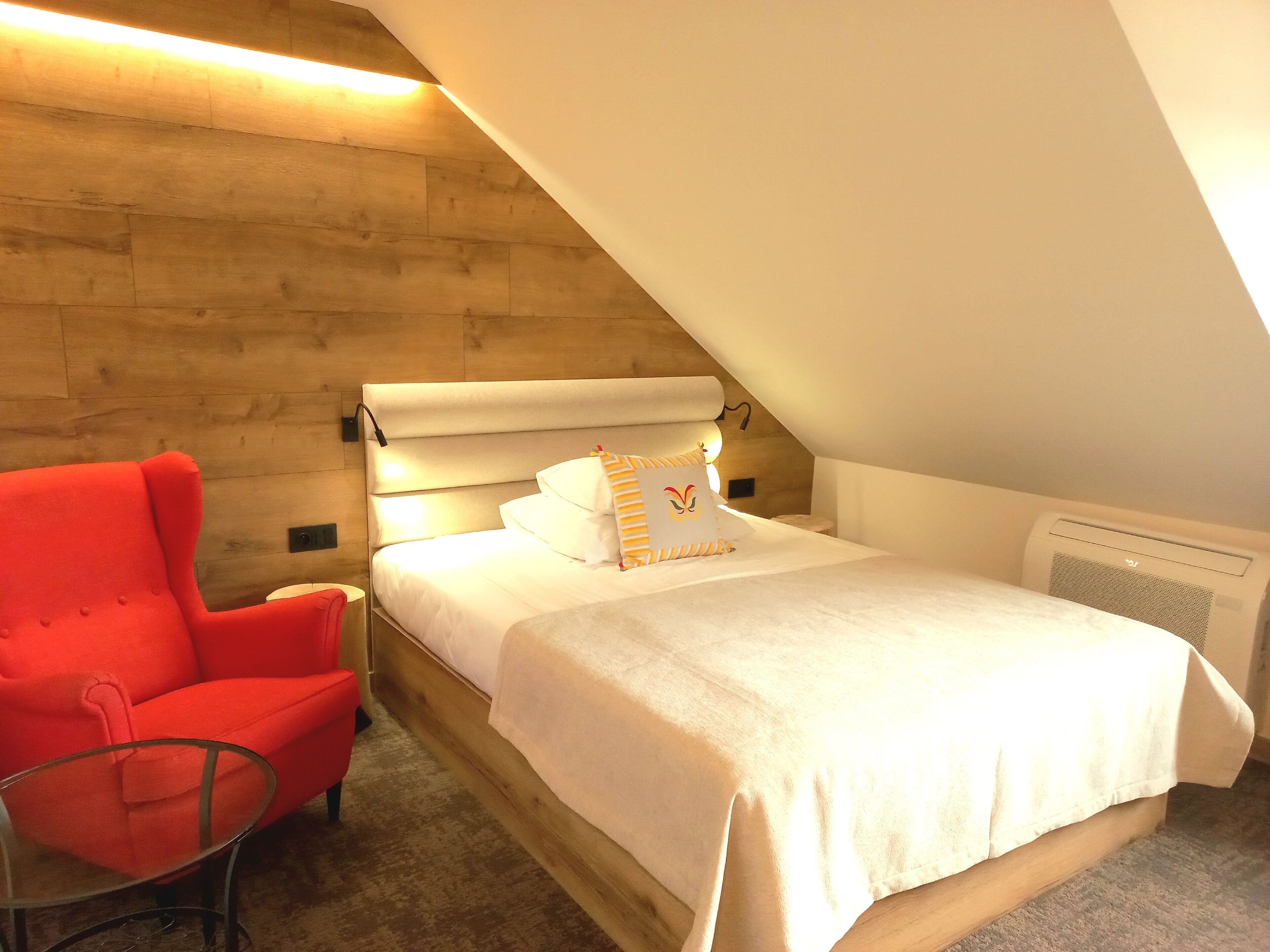 A bedroom with a wooden wall, a bed with white bedding, a red chair, and a ceiling fan.