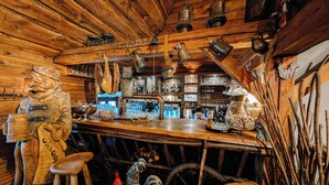 A rustic wooden bar with a wooden bear figure, a spinning wheel, and various bar tools.