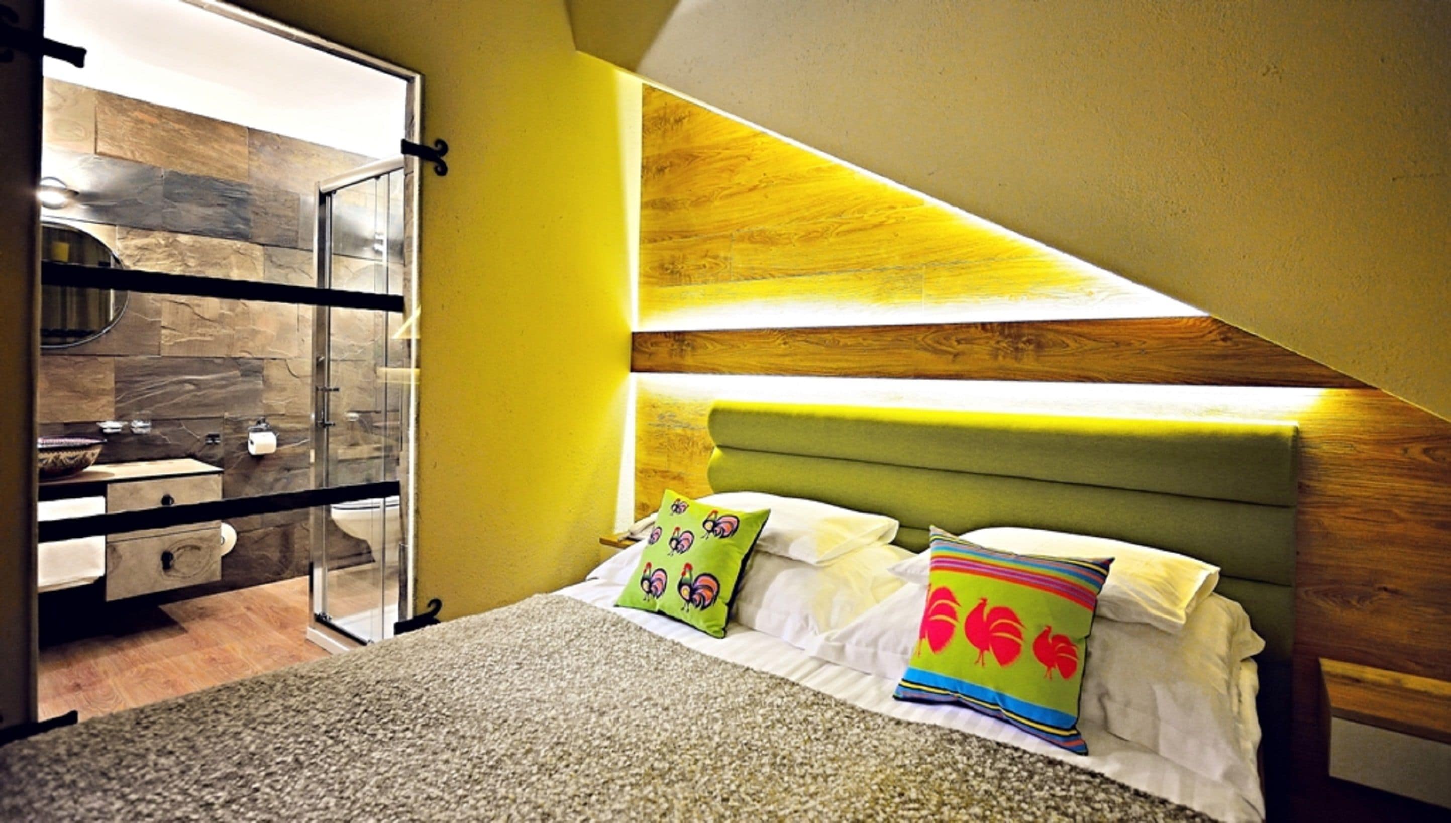 Une chambre à coucher avec un lit, deux oreillers, une tête de lit verte, un mur en bois et une salle de bain dotée d’une porte de douche en verre.