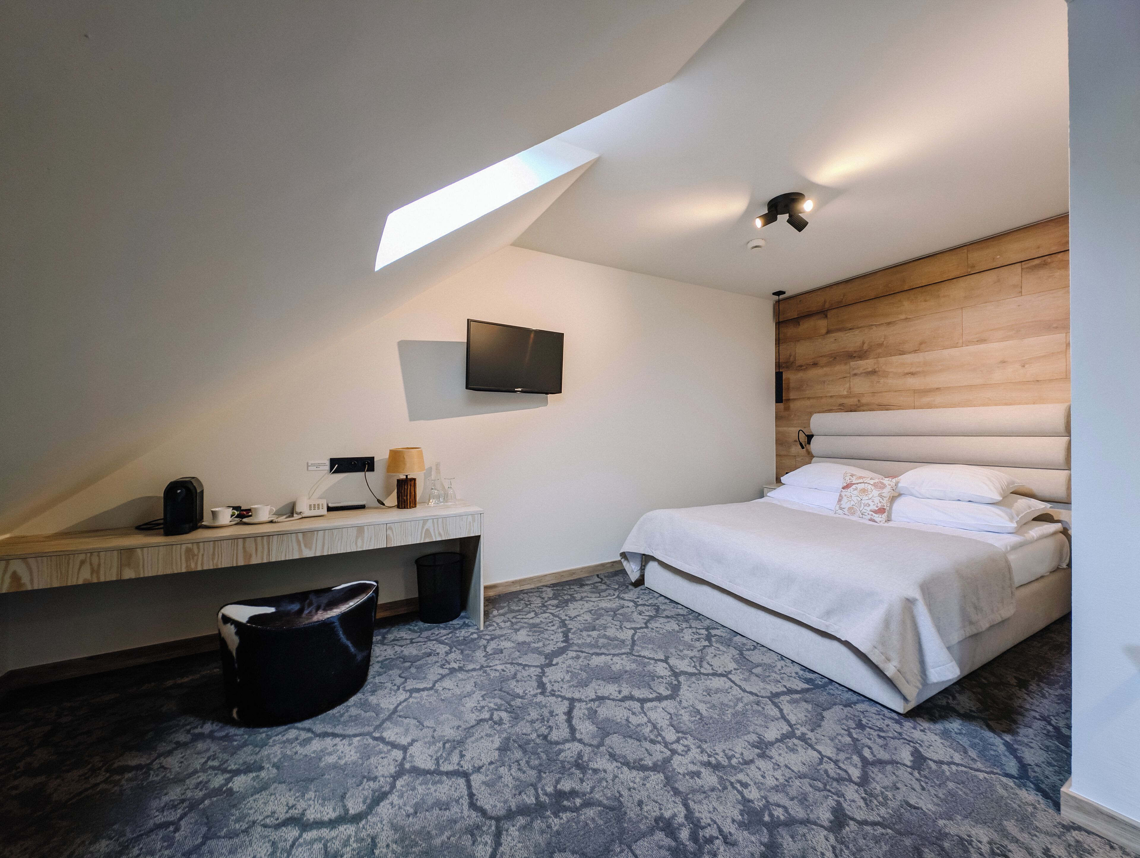 A hotel room with a bed, a desk with a lamp, a TV, and a large window.