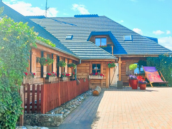 A wooden building with a sloped roof, a wooden fence, and hanging flower baskets.