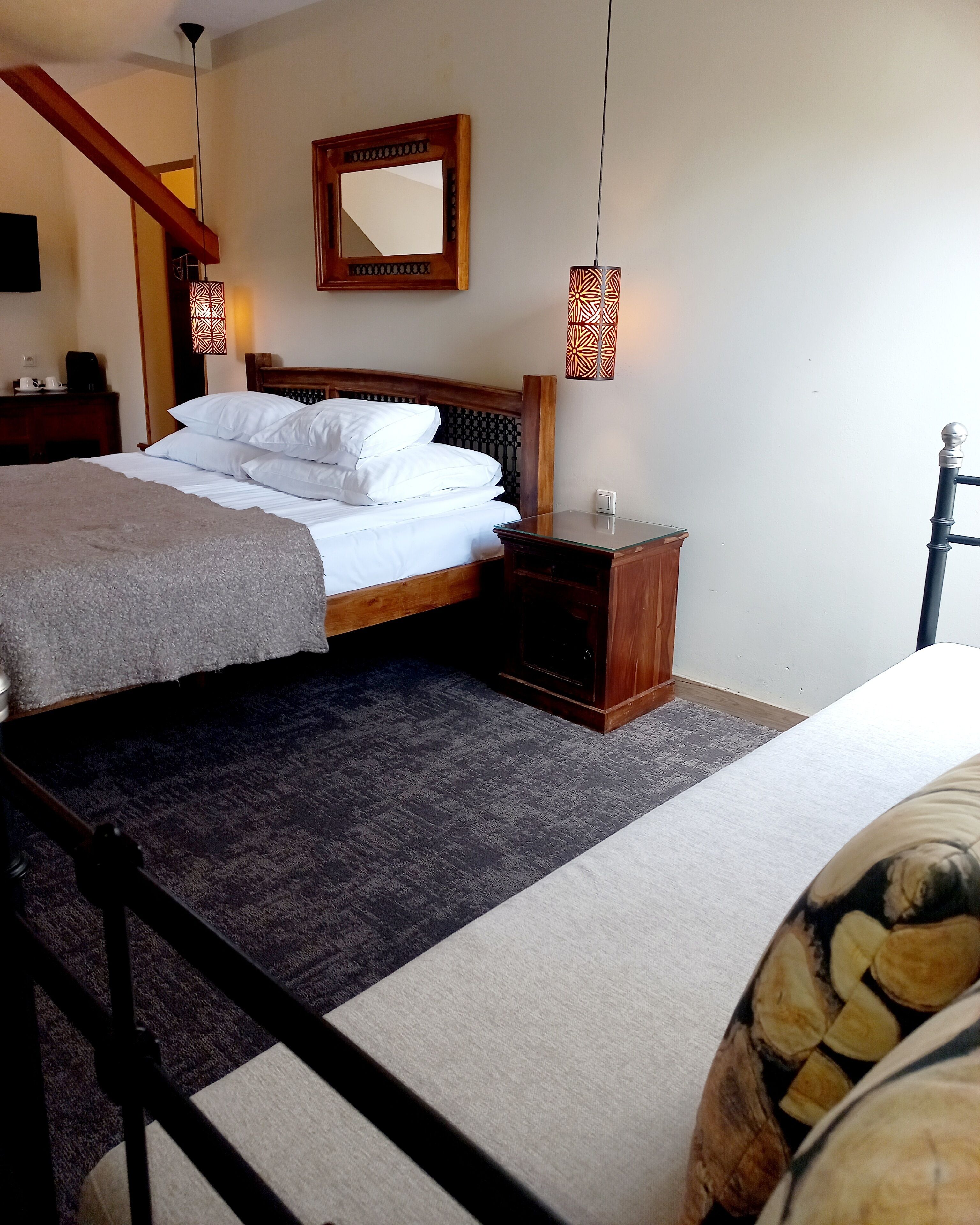 Un dormitorio con cama, mesitas de noche, una cabecera de madera, un espejo y lámparas colgantes.