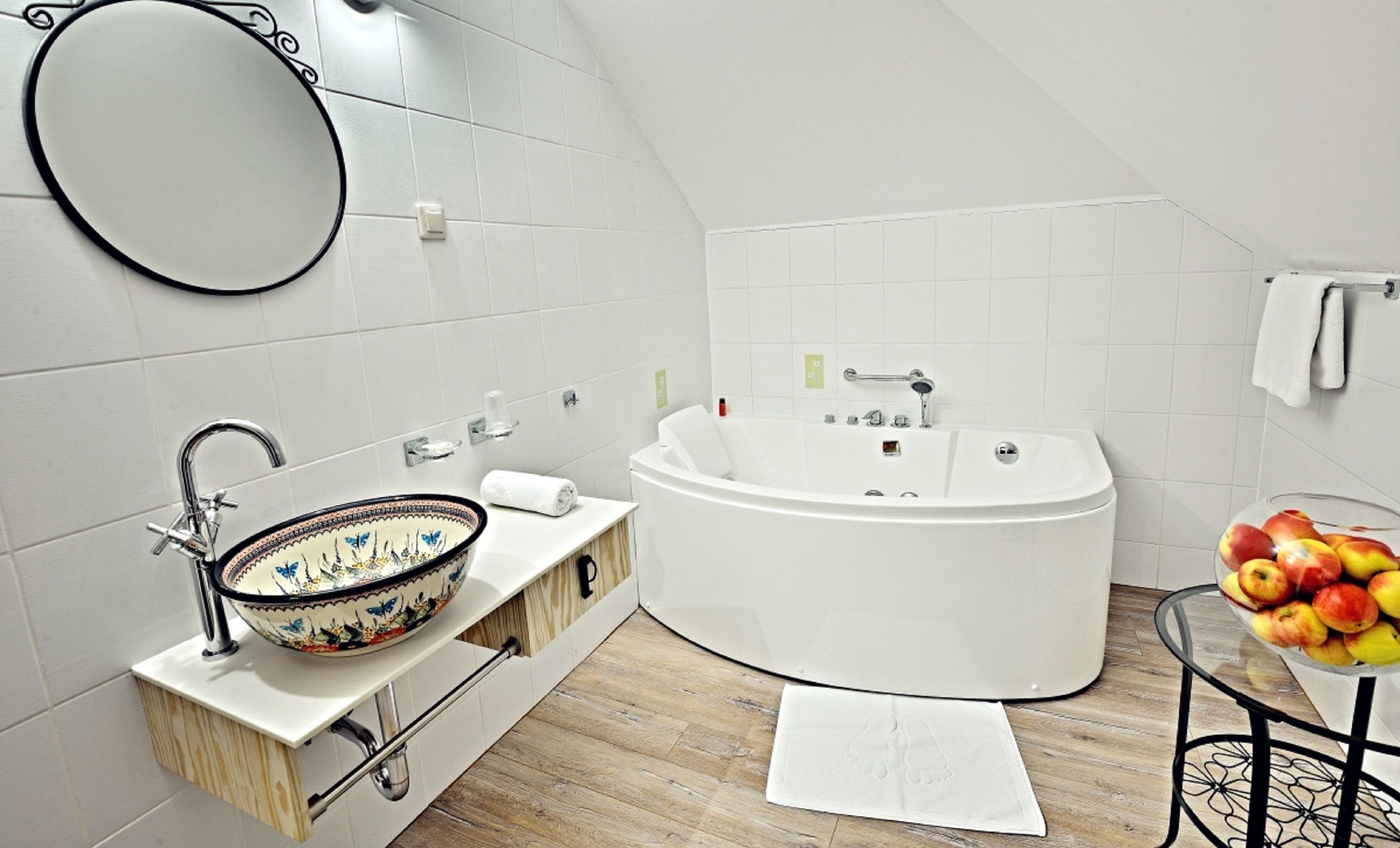 A modern bathroom with a freestanding bathtub, a large round mirror, a sink with a decorative bowl, and a small table with fruit.