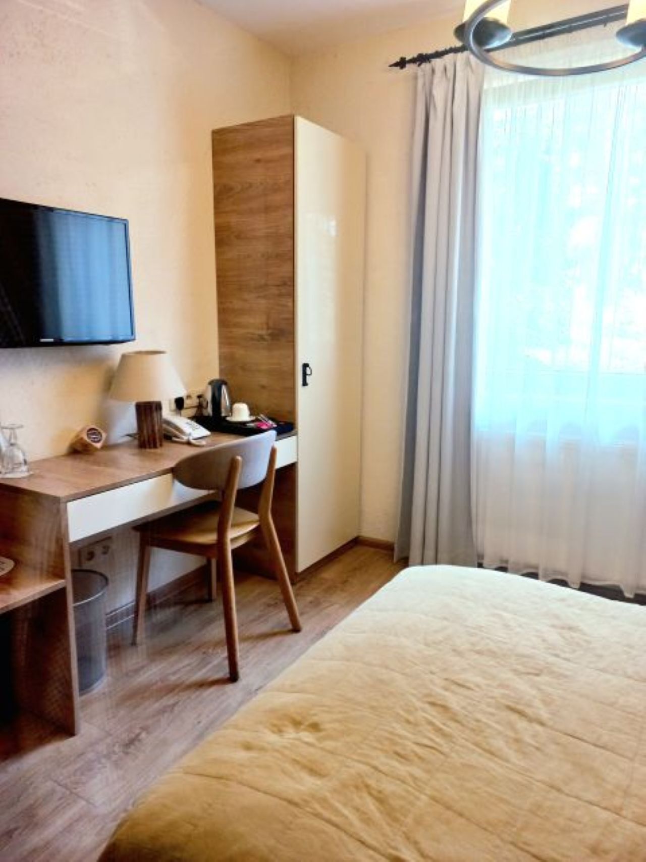 A hotel room with a bed, a desk with a chair, a television, and a window with curtains.