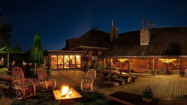 A rustic wooden building with a large open patio area, furnished with wicker chairs and a central fire pit.
