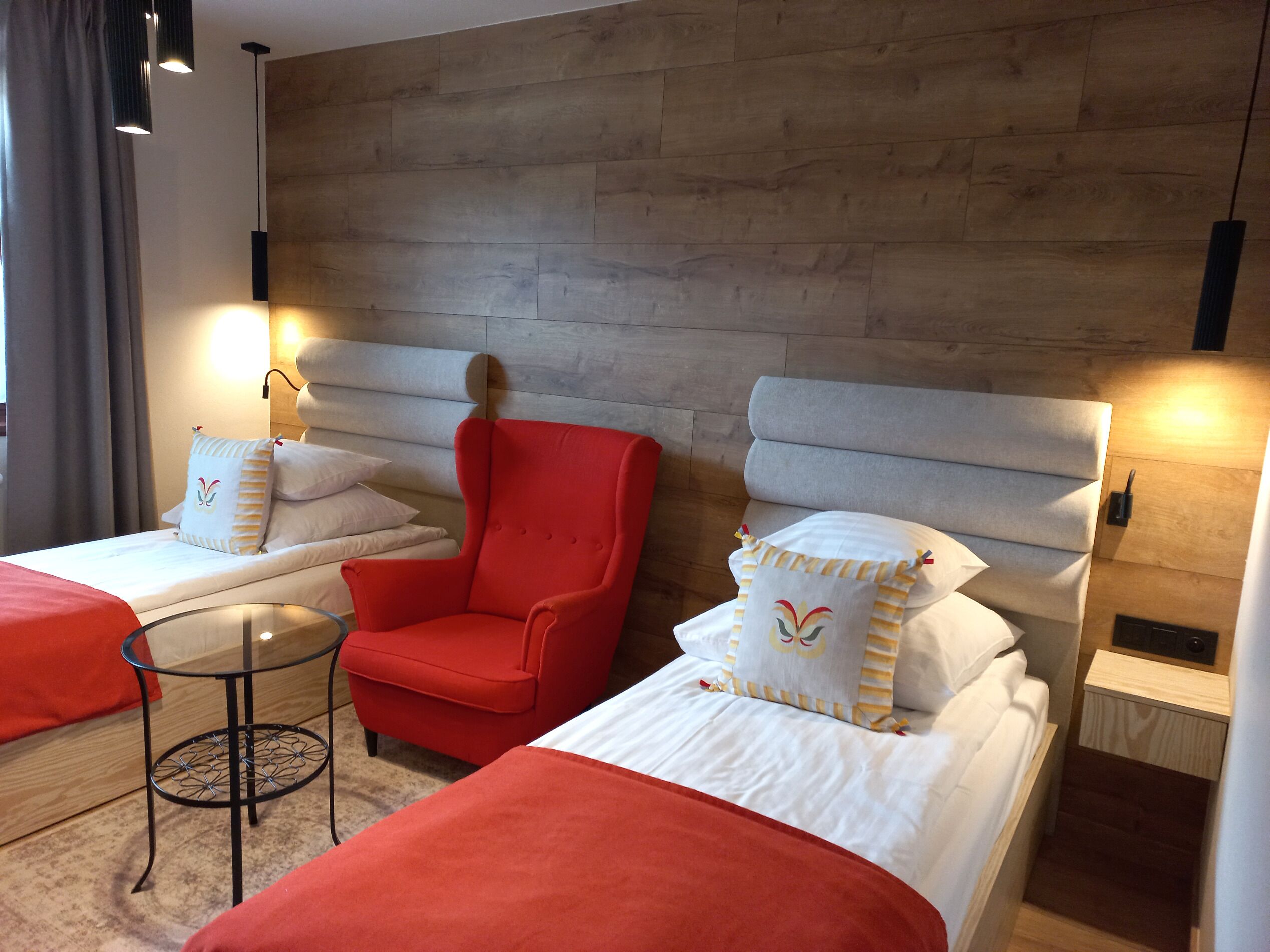 Ett hotellrum med två sängar, en röd fåtölj, ett litet runt bord och en sänggavel i trä.