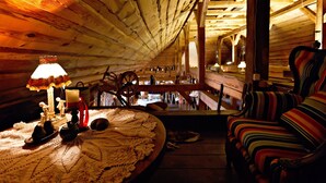 A cozy attic room with wooden beams, a patterned sofa, a table with a lace tablecloth, and a lit lamp.